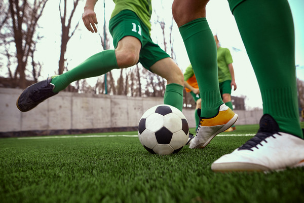 na zdjęciu fragment meczu piłki nożnej, zawodnicy w zielonych strojach, pomiędzy nimi piłka